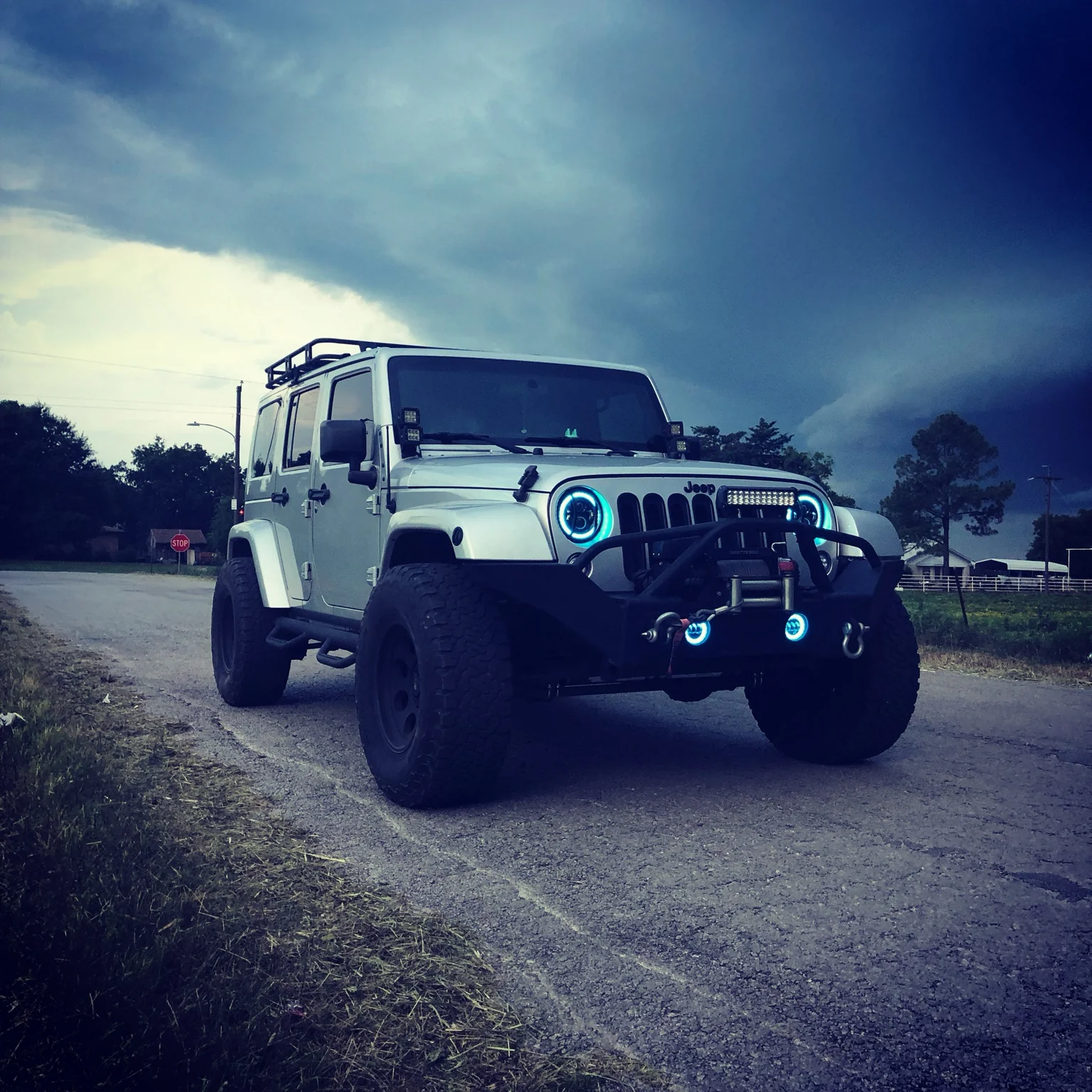 White Jeep beneath storm clouds with auxiliary lighting